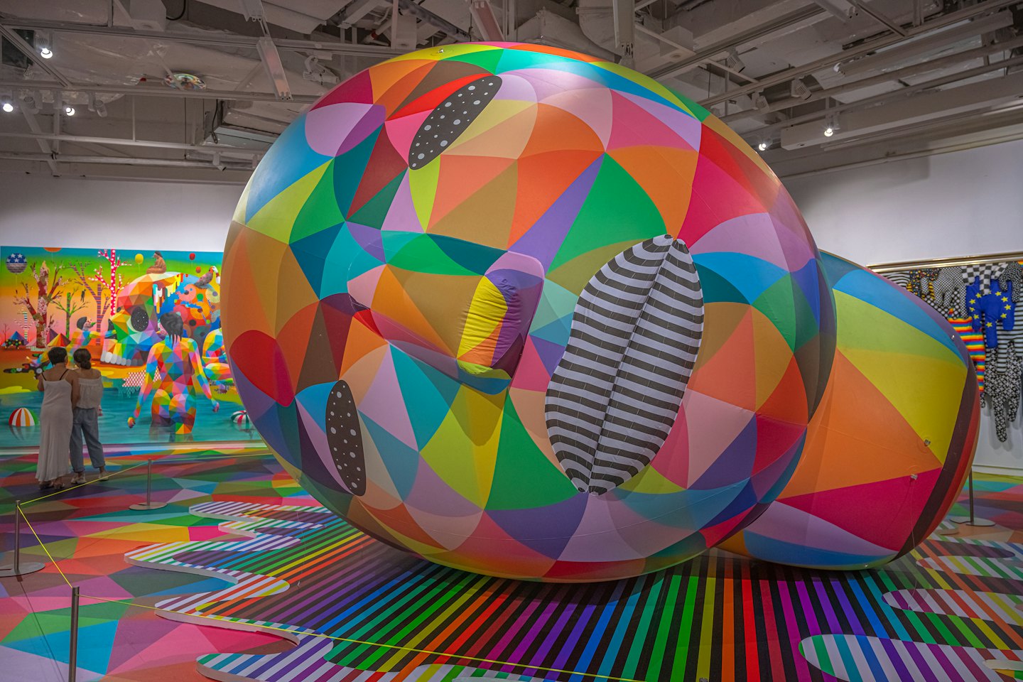 Two women view a painting behind a patterned spherical sculpture.