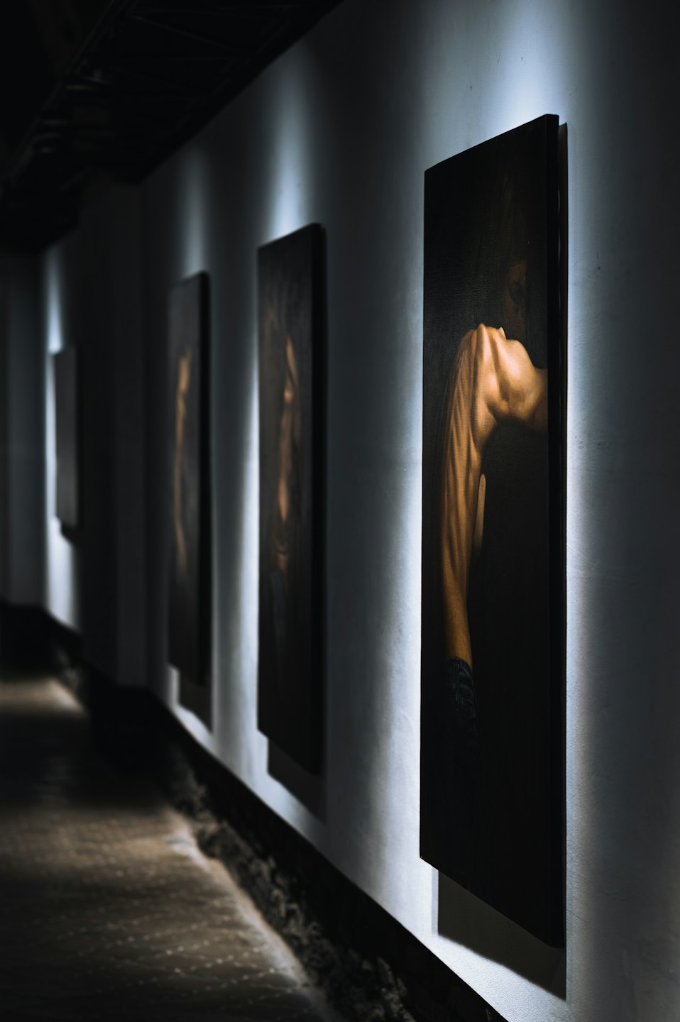 Abstract paintings hang along a narrow art gallery corridor.