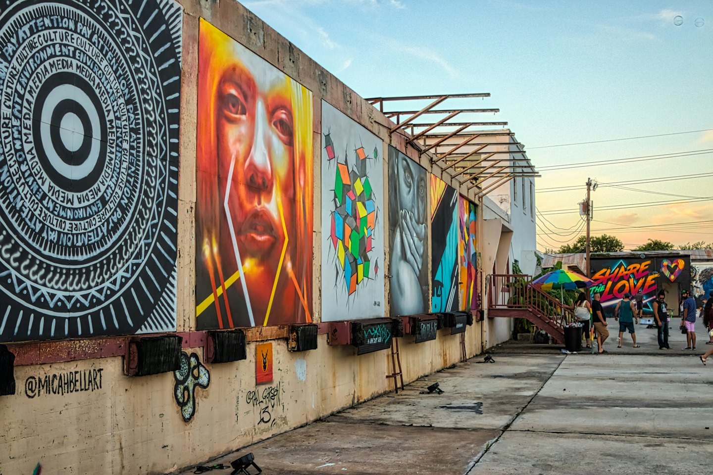 People gather near colorful murals painted on an outdoor concrete wall.